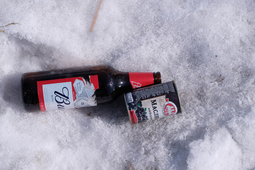 Пустая бутылка из-под пива и пустая банка из-под маслин на снегу