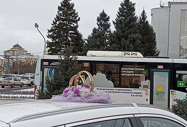 Виды Улан-Удэ. Кольца на крыше свадебной машины на фоне автобуса МУП "Городские маршруты"  с цитатой Путина. Осень 2023 года