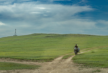 ��������. ������ �� ��������� �������� �� �������� ������. A Mongolian man on a motorcycle is moving along a country road.