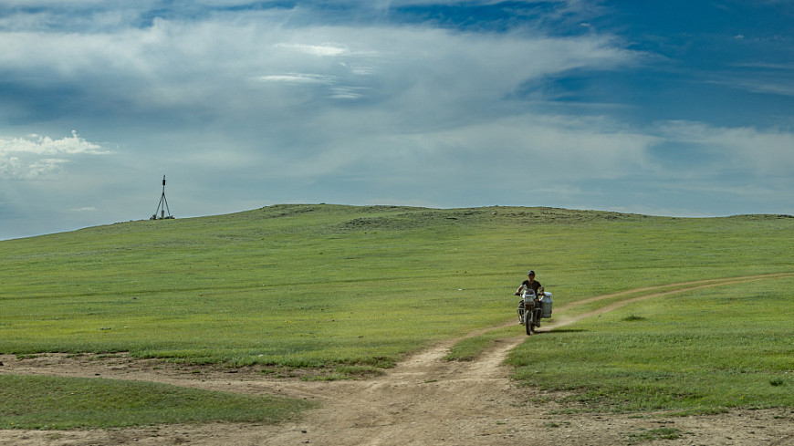 ��������. ������ �� ��������� �������� �� �������� ������. A Mongolian man on a motorcycle is moving along a country road.