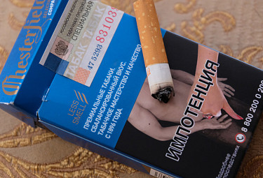 Курение вредит. Потушенный окурок на пачке сигарет с антитабачной фотографией об импотенции